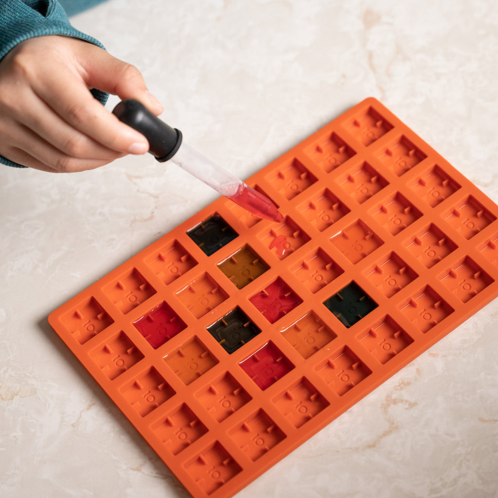 Orange silicone mold with colorful compartments on a light surface