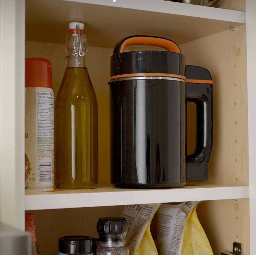 Black thermos with orange accents on a kitchen shelf with various items.