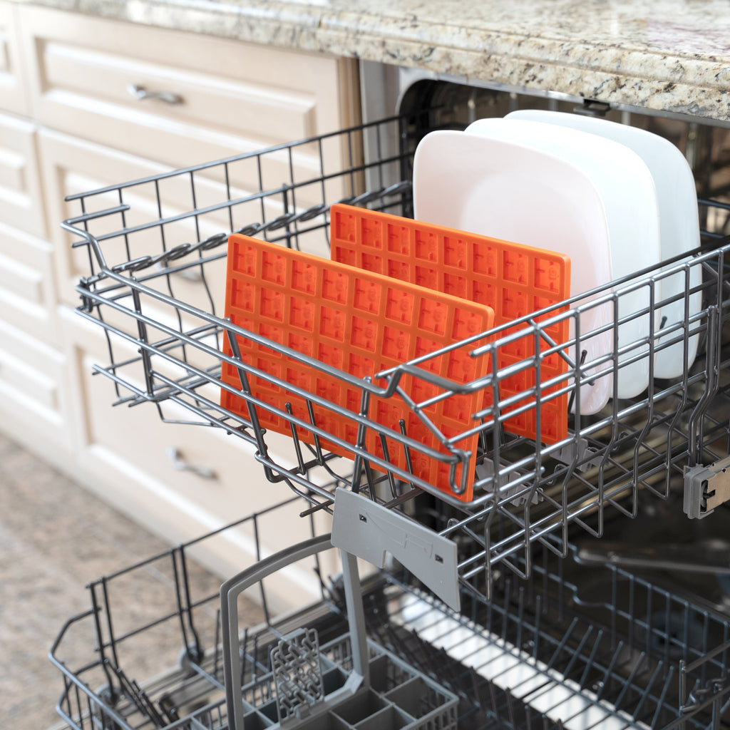Dishwasher with a rack containing orange silicone baking mats and a white plate.