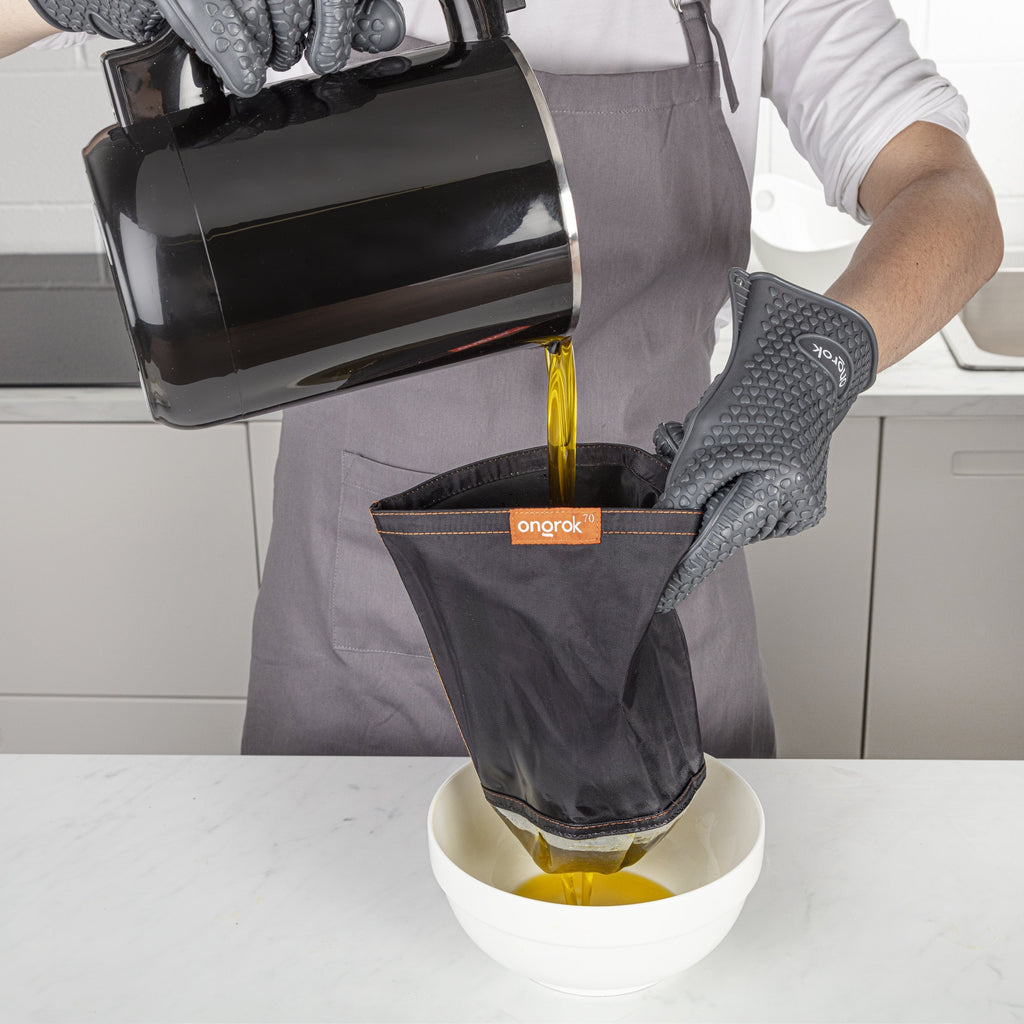 Person pouring liquid from a pot into an orange-colored kitchen tool, wearing gloves and an apron.