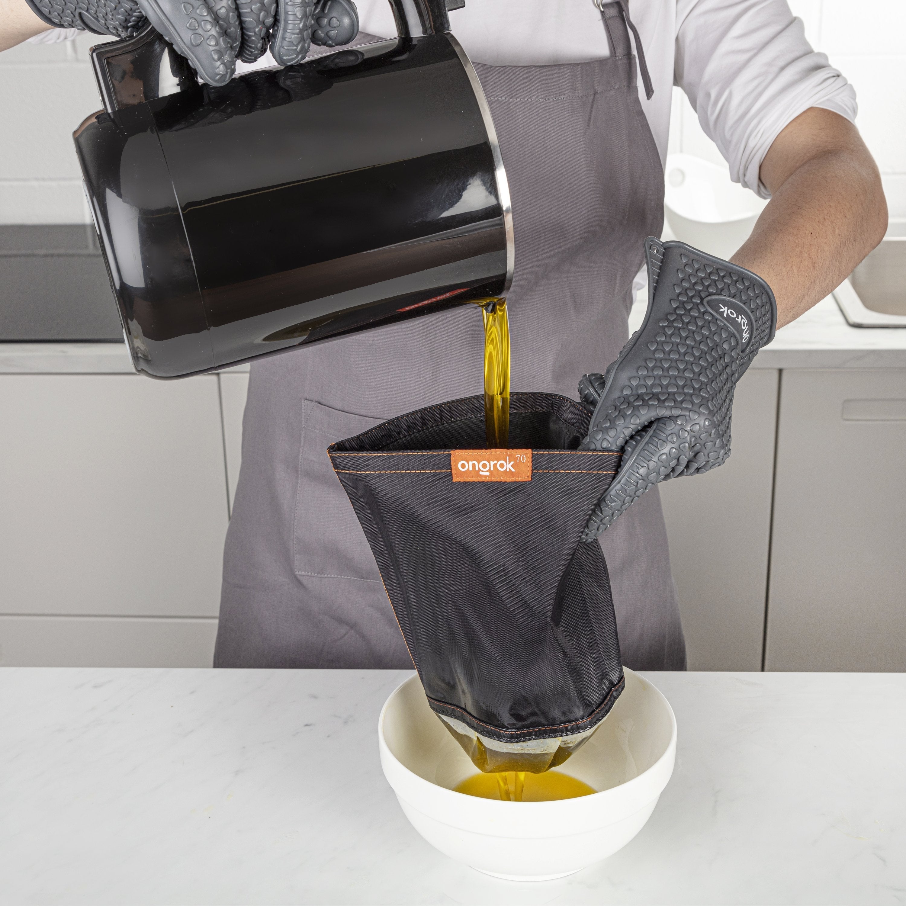 Person pouring liquid from a pot into an orange-colored kitchen tool, wearing gloves and an apron.