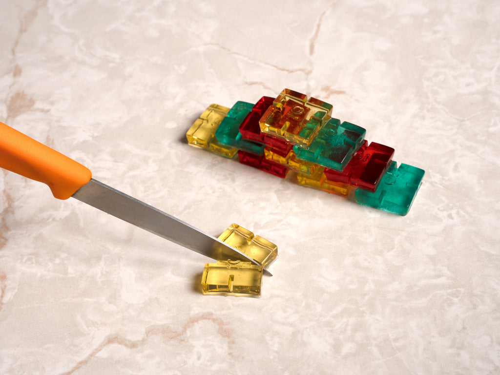 Colorful gummies being cut with a knife on a light-colored surface