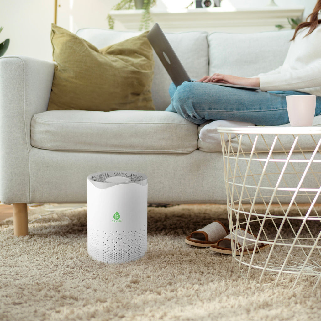 Air purifier on a carpeted floor with a person using a laptop in the background