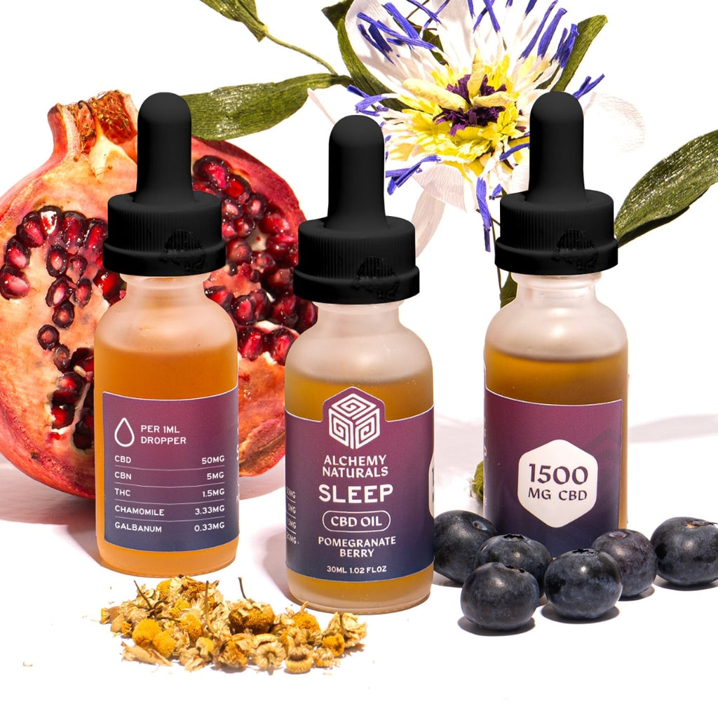 Three bottles of Alchemy Naturals CBD oil with natural elements like pomegranate, blueberries, and flowers on a white background.