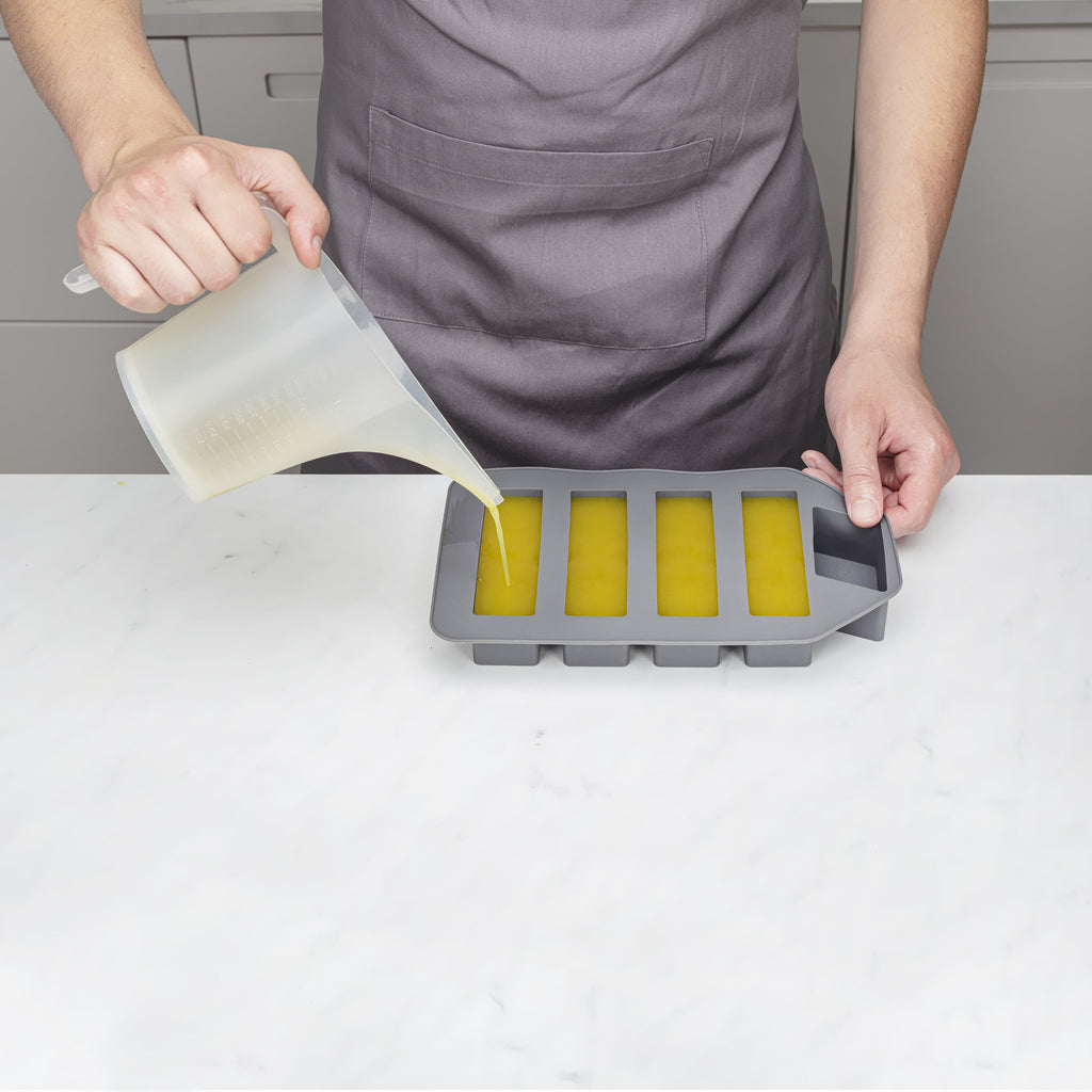 Person pouring a liquid into a silicone mold on a white surface.