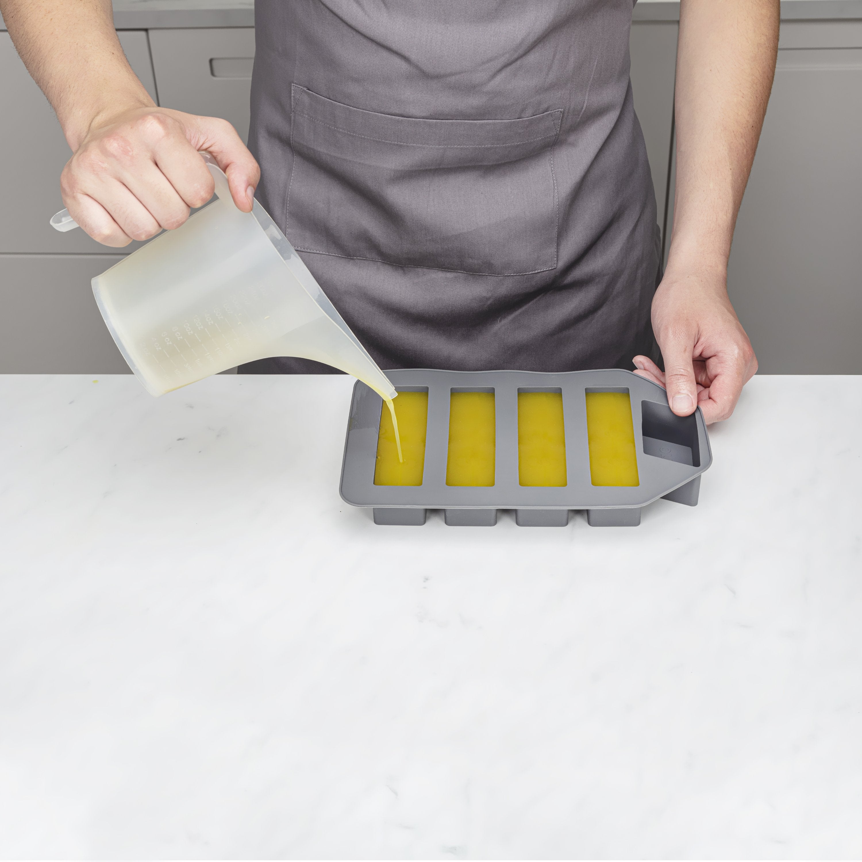 Person pouring a liquid into a silicone mold on a white surface.
