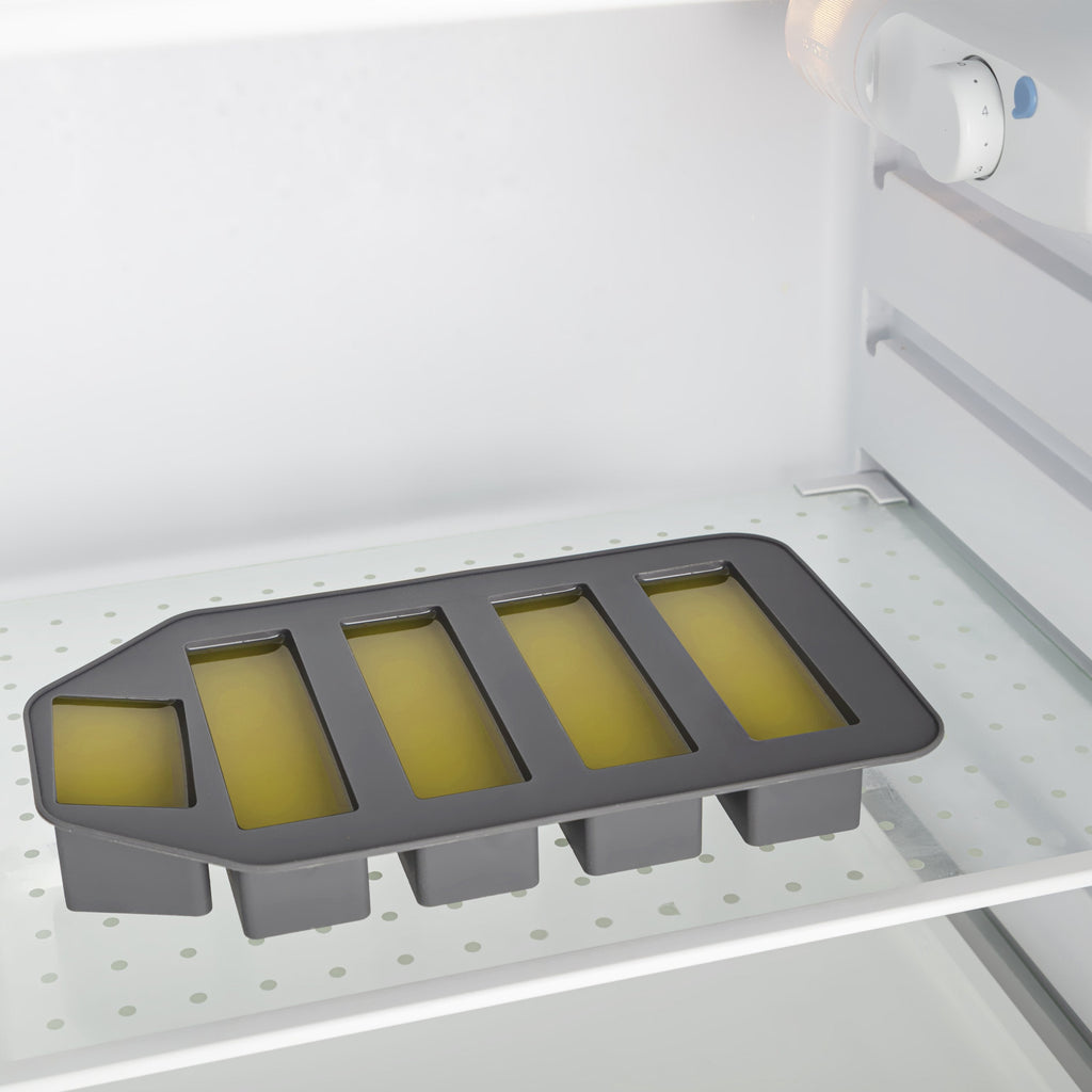 Gray silicone ice cube tray with yellowish substance in a refrigerator.