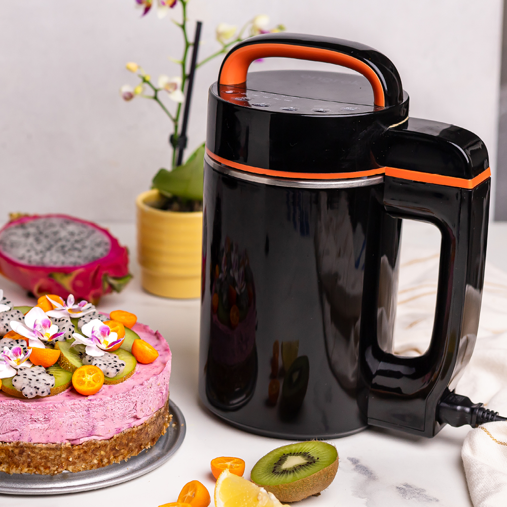 Black and orange kitchen appliance on a table with a cake and fruit